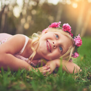 Shot of a happy little girl looking at the camera while lying on the ground outside in nature